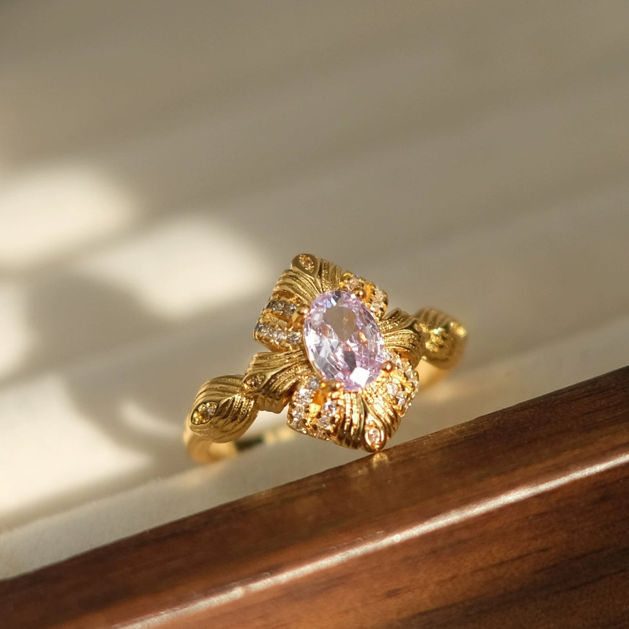 Gold ring with a pink gemstone on a wooden surface, branded 'SW accessories'.