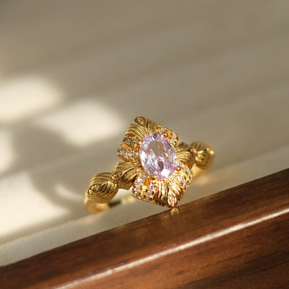Gold ring with a pink gemstone on a wooden surface, branded 'SW accessories'.